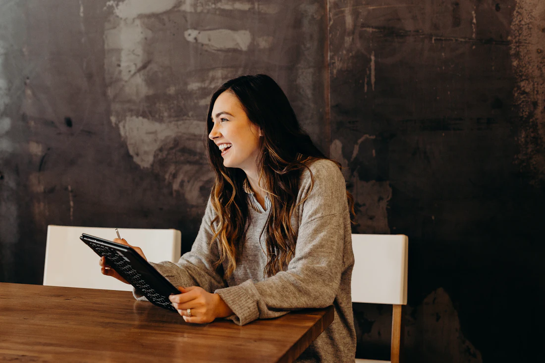 Mulher sorrindo enquanto consulta um tablet em uma mesa de trabalho